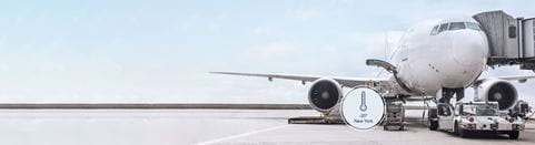 A large commercial aircraft is parked at an airport gate, connected to a jet bridge, with ground handling equipment nearby.