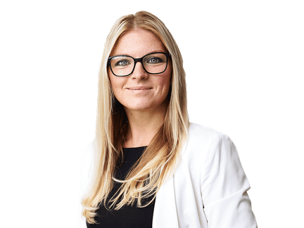 Donna professionale con capelli biondi lunghi e occhiali, indossa un blazer bianco sopra una maglia nera, in piedi e sorridente con sicurezza su sfondo bianco