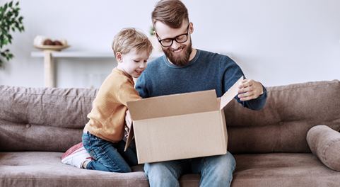 Mann und Kind entpacken auf einem Sofa ein Paket