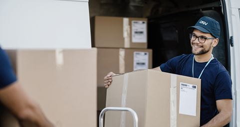 DSV:n siniseen paitaan ja lippalakkiin pukeutunut mies pitää isoa pakettia sylissään.