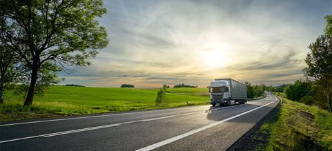 Rekka ajaa maantiellä, ja aurinko laskee taustalla.