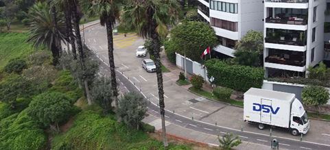 Camión de DSV servicio de distribución en Lima en camino cerca de la costa con palmeras y edificios de fondo | DSV Perú