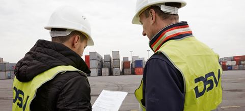 Personal de DSV leyendo un documento en el puerto, frente a contenedores marítimos