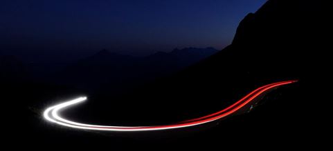 Haz de luz blanco con rojo, simulando un camino recorrido en una carretera entre las montañas por la noche.