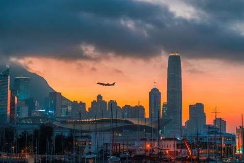 Imagen de un avion aterrizando a un aeropuerto durante un atardecer naranja con la silueta de los edificios de una ciudad en el fondo