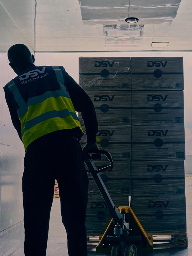 A DSV worker loads stacked boxes onto a truck with a pallet jack.