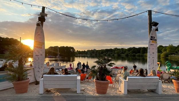 Personen sitzen auf Bänken am Strand zwischen mit DSV Logo bedruckten Surfboards