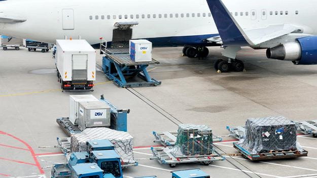 Air cargo containers and freight pallets being prepared for loading beside a commercial aircraft at the airport.