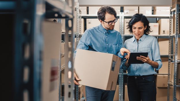 Female inventory manager shows digital tablet information to a worker holding cardboard box