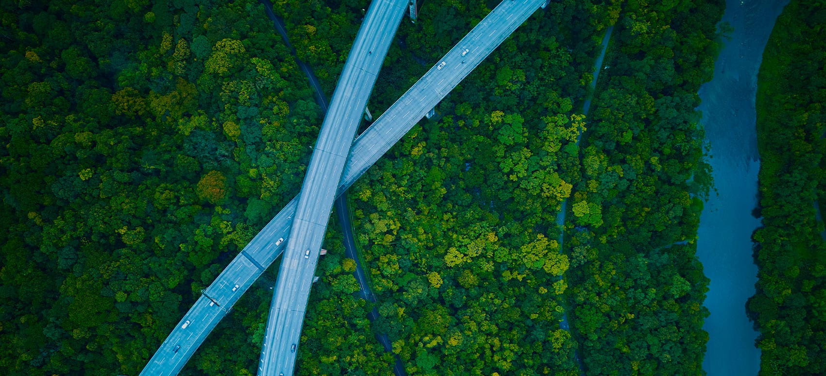 Eine Luftaufnahme von zwei Autobahnen, die sich über einem grünen Wald und einem Fluss kreuzen.