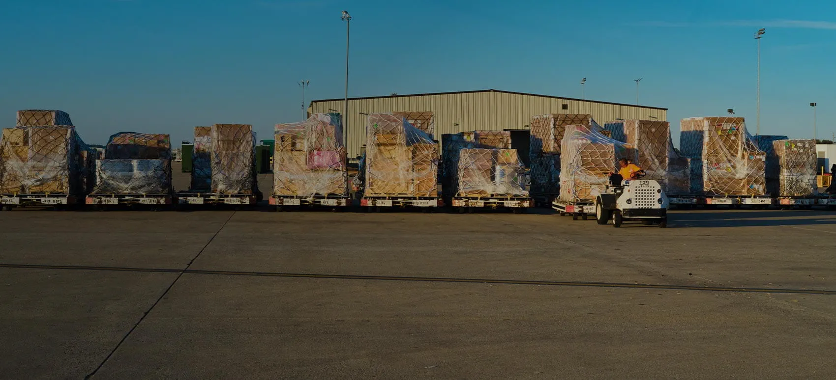 A line of palletized cargo on dollies awaits transport at an airport.