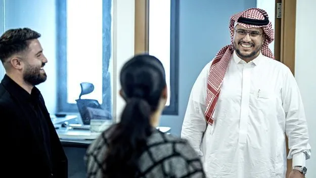 Three colleagues smiling and greeting each other in DSV Jeddah Office, engaged in a friendly conversation