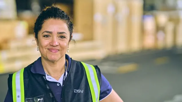 A smiling woman wearing a DSV vest in a warehouse setting.