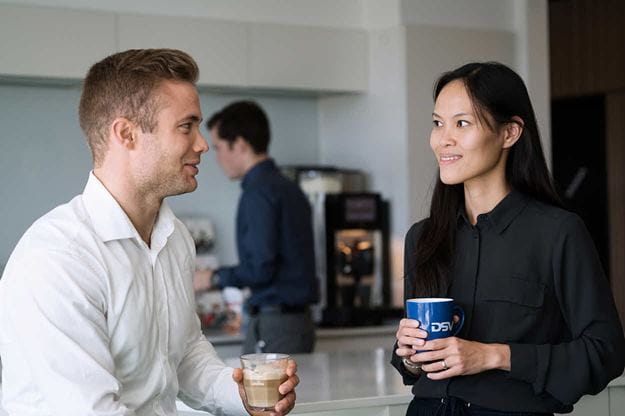 A man and a female drinking coffee by the coffee machine