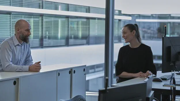 A man and a woman are engaged in conversation in a modern office setting.