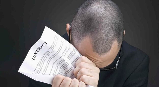 A man showing frustration and holding a contract to his head