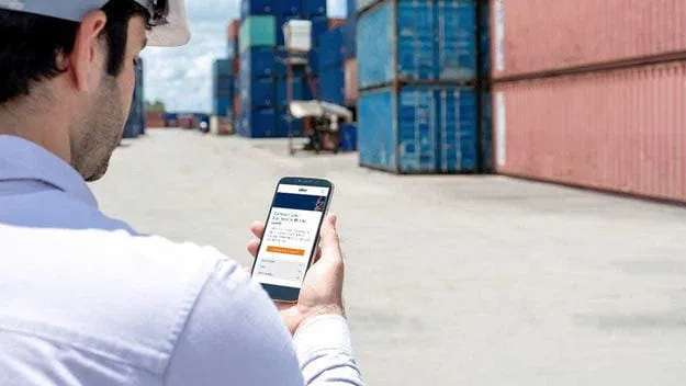 Shipping officer standing front side of container and using smart phone to contact his team at container yardDSV has flexibility and visibility