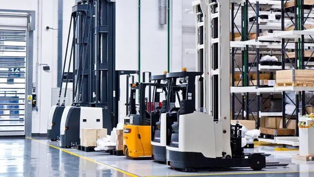 A row of reach trucks parked in a warehouse aisle, with tall shelving in the background.