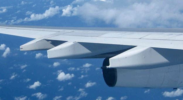 An image of an aircraft wing against a backdrop of blue sky and scattered clouds.
