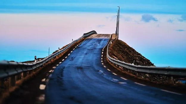 Coastal road curving over a hill under a pastel sky