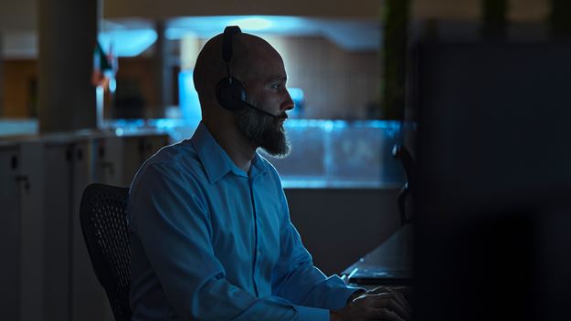 Oficinista de sexo masculino con un auricular que mira una pantalla de computadora