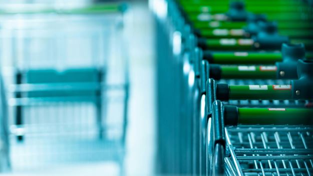 A row of colourful puffer jackets hanging on black hangers, displayed on a wooden rack in a storefront window.