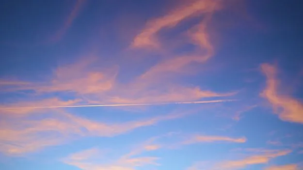 Colourful sunset sky with soft pink clouds and a thin aircraft trail