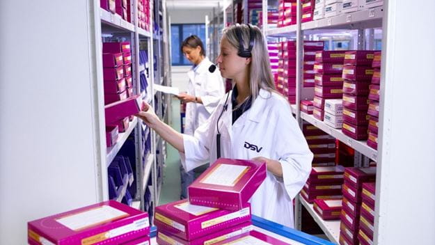 Personal en bata organizando productos farmacéuticos en un almacén DSV