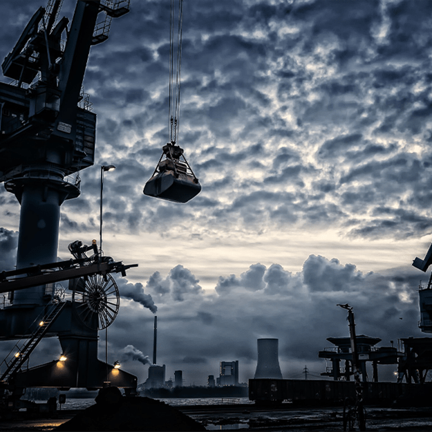 A heavy-duty industrial crane lifting a cargo load against a dramatic cloudy sky, highlighting the scale of port operations.