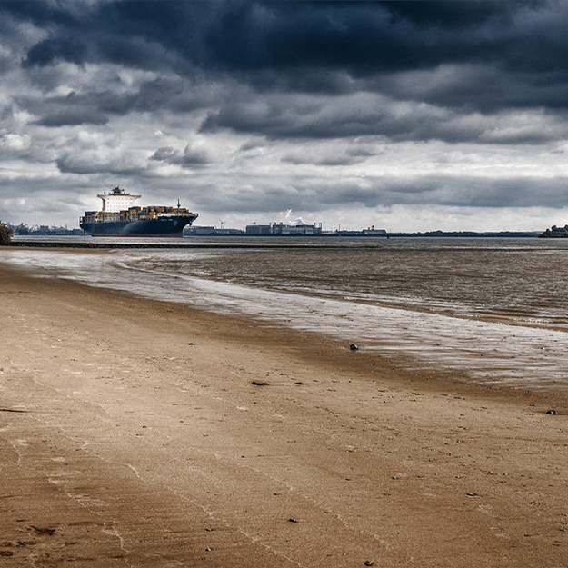 Large cargo ship sailing near the shore under a cloudy sky