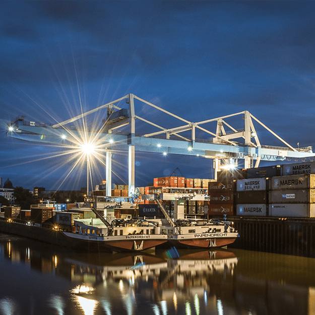 Nighttime view of a shipping port featuring large cranes and stacked shipping containers