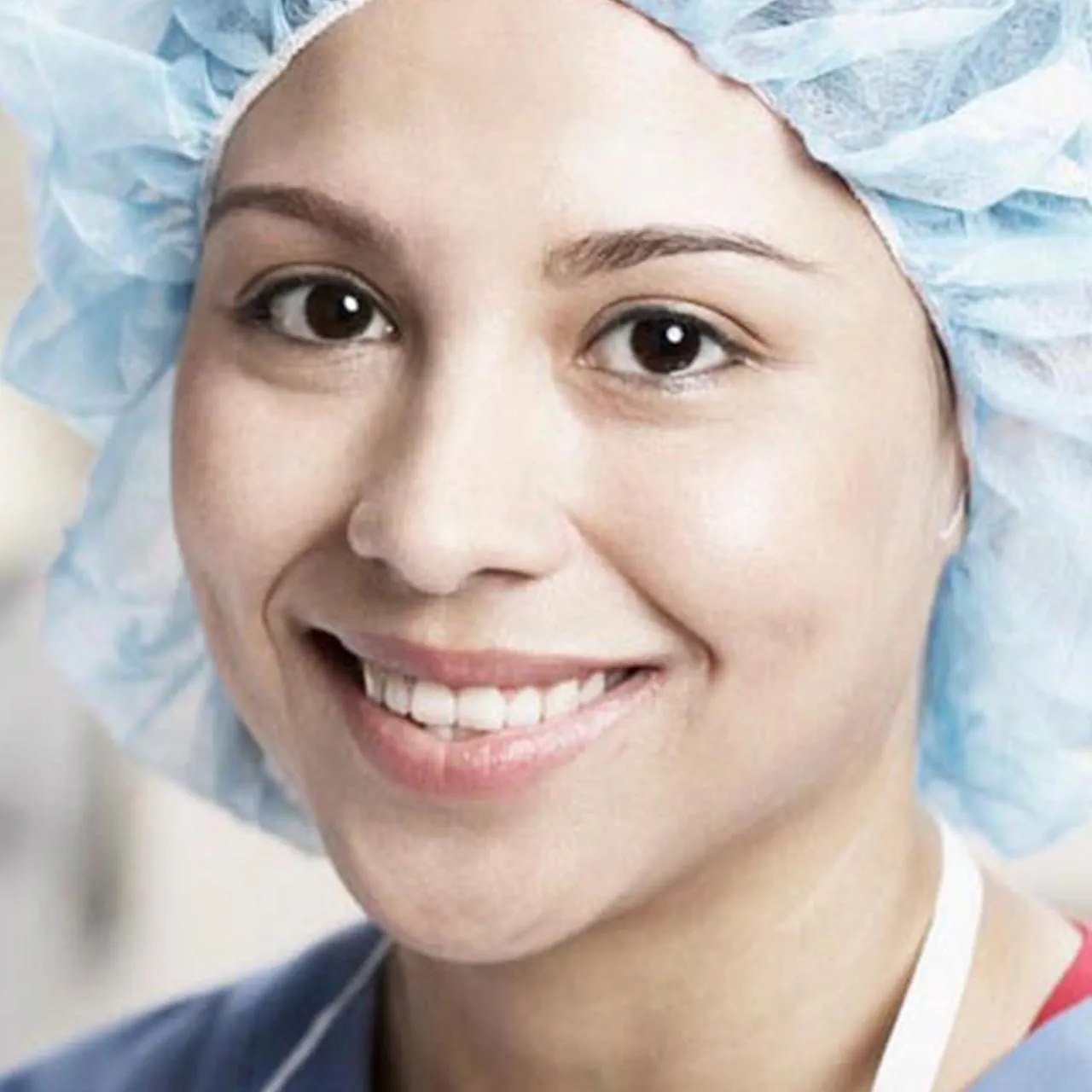 "A close-up of a smiling healthcare professional wearing a light blue surgical cap and uniform