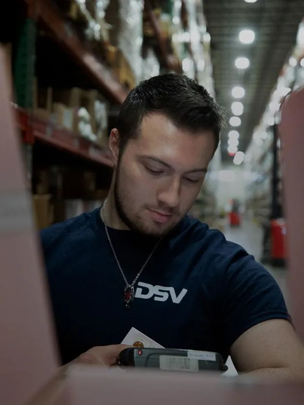 A male DSV staff member is printing package labels in a warehouse.