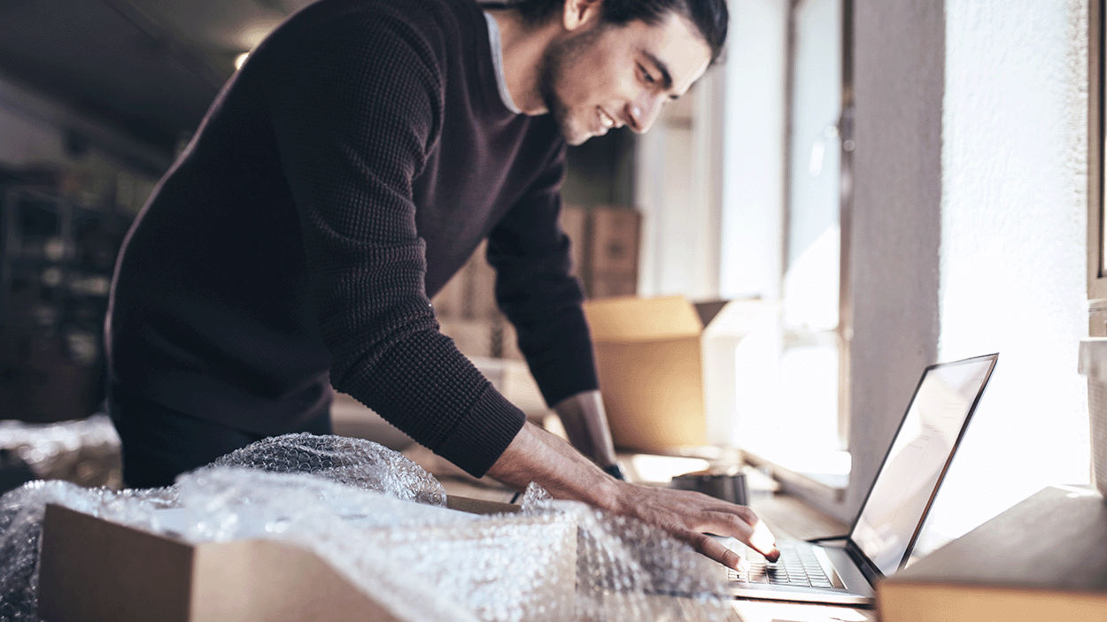 Uomo che lavora su un computer portatile con pacchi pronti per essere imballati accanto a lui