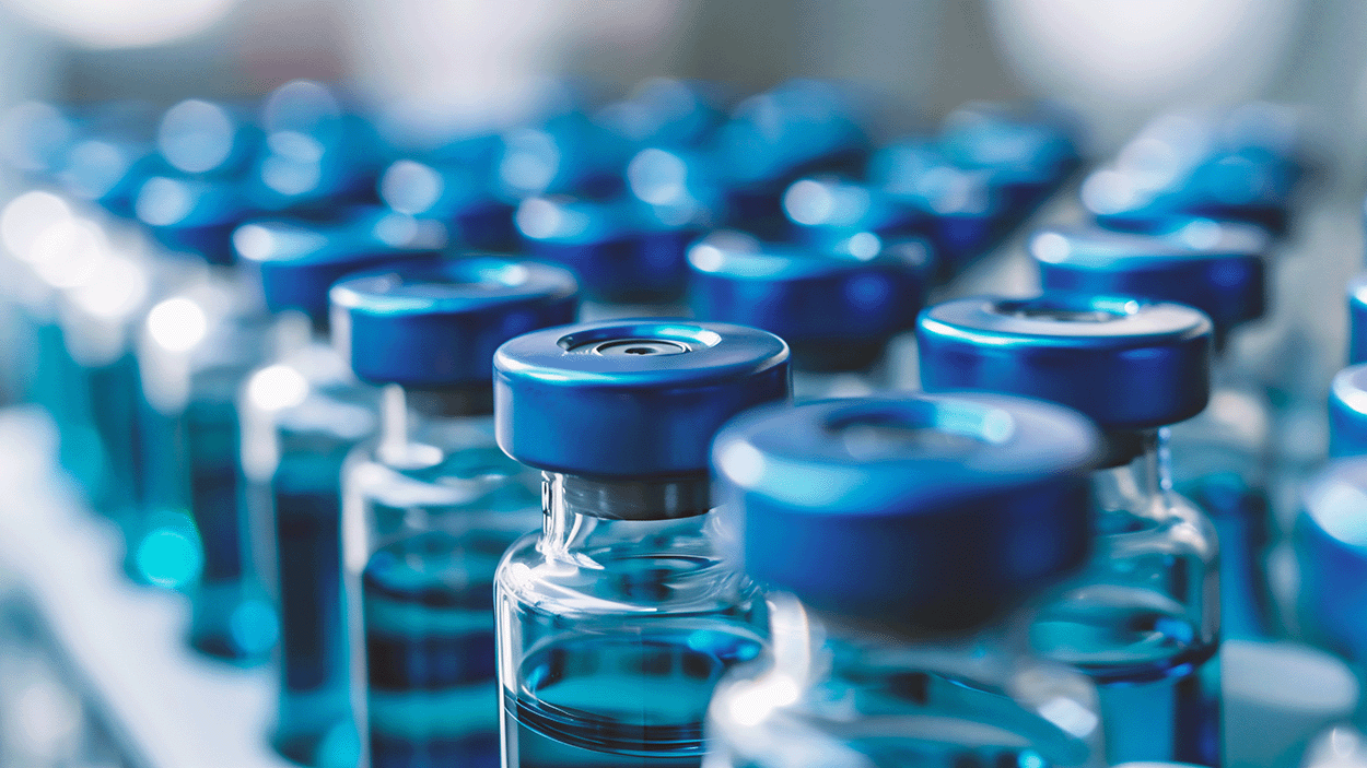 Close-up of multiple sealed medical vials with blue caps arranged in rows in a laboratory or pharmaceutical production setting